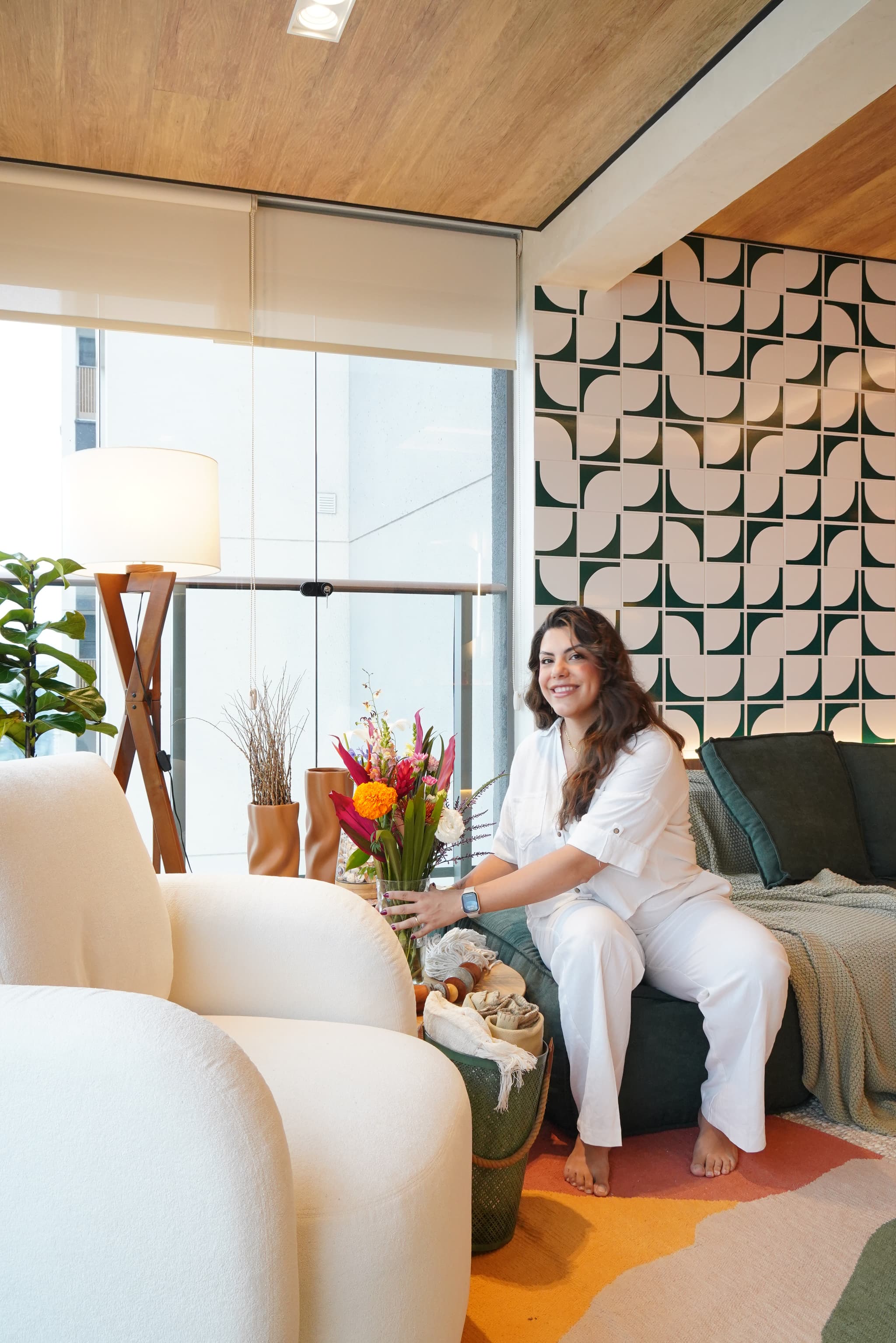 Sala de estar com parede de azulejos geométricos verdes e brancos, forro de madeira, sofá curvo claro e tapete colorido