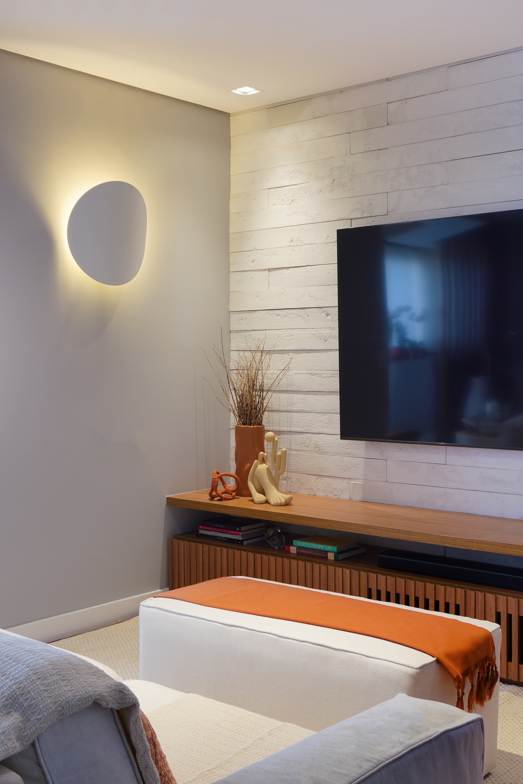 Sala de TV com painel claro, arandela redonda e rack de madeira