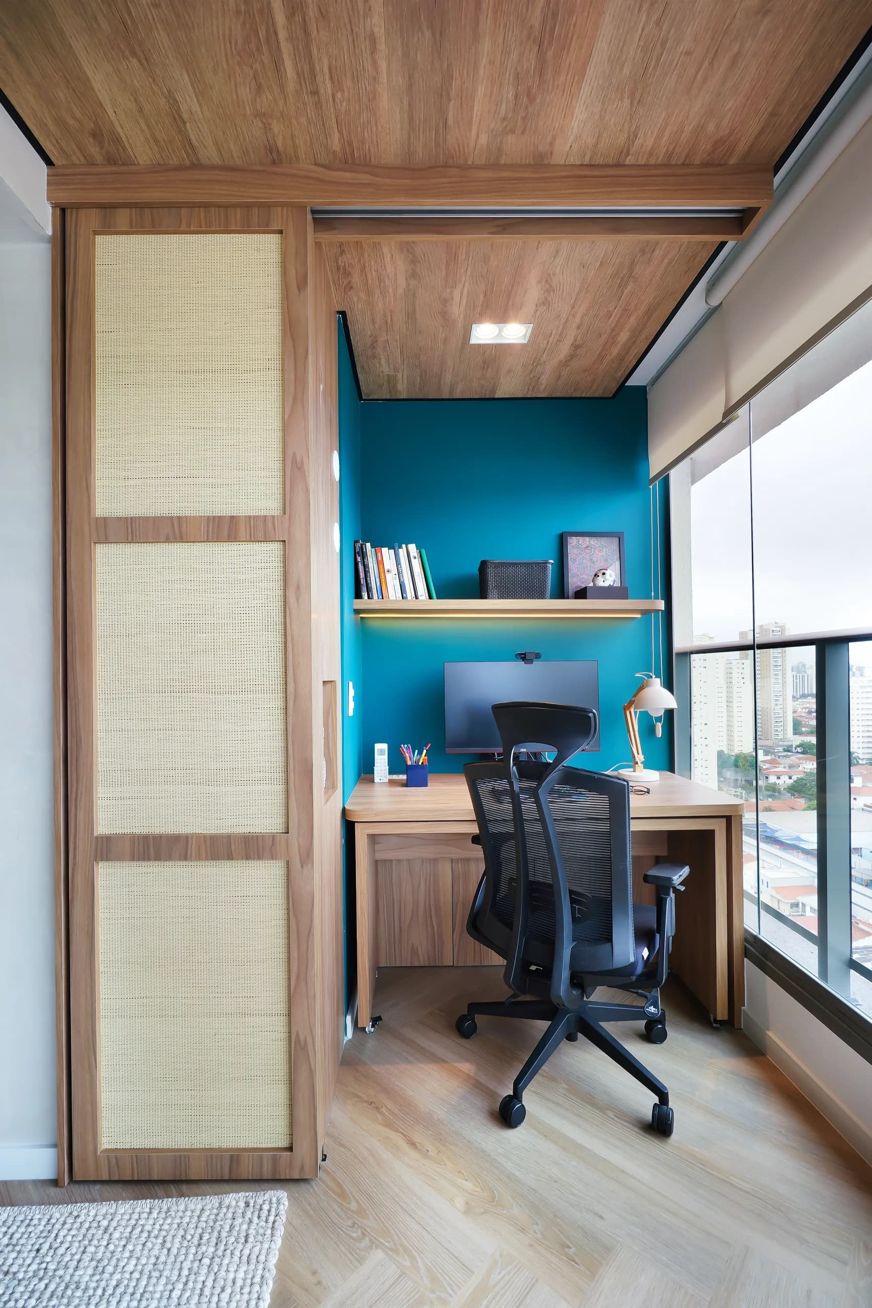 Home office escondido atrás de painéis deslizantes de palhinha, com parede azul e vista da janela