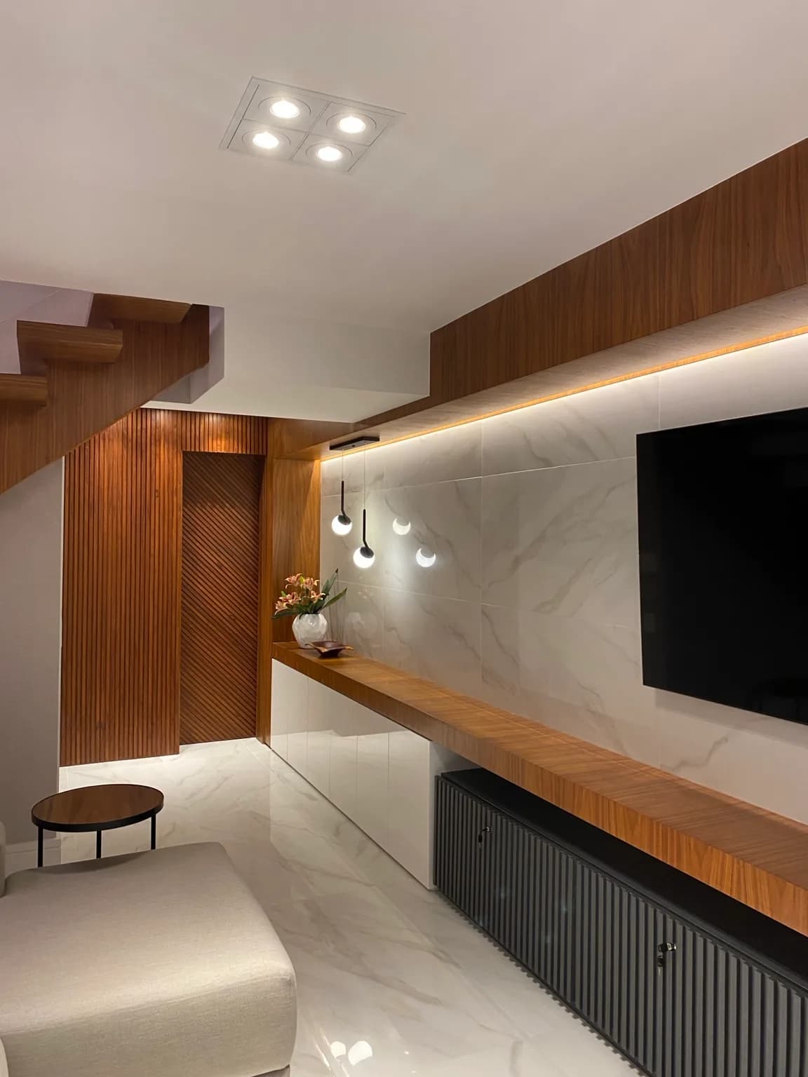 Parede de mármore com TV e marcenaria de madeira na sala, vista do hall da escada