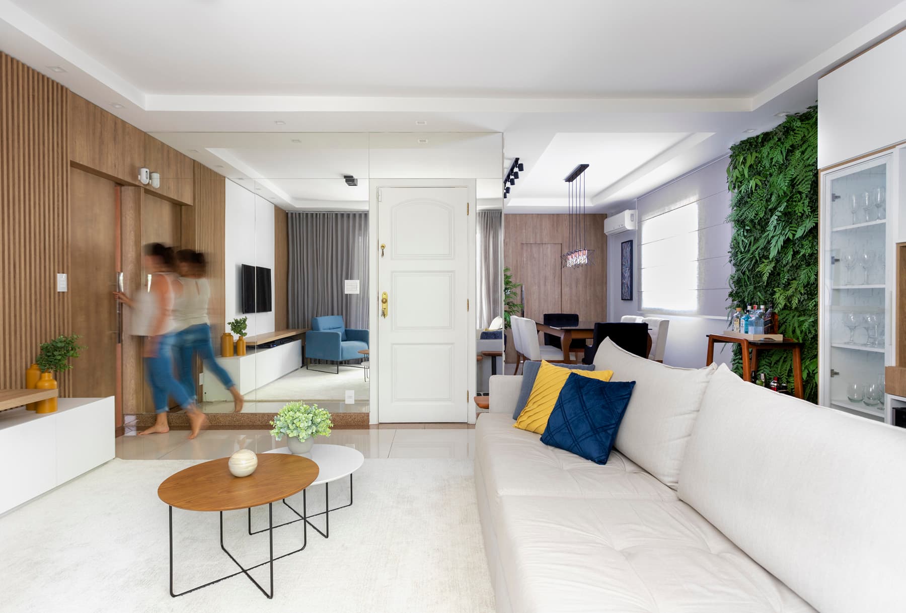 Sala de estar com sofá claro, mesas de centro e jardim vertical em apartamento reformado