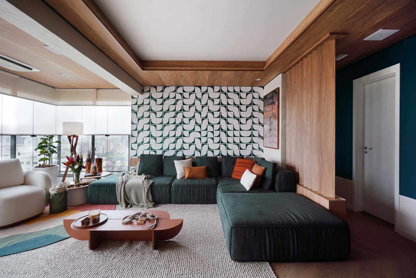A mesma sala pronta, fotografada: sofá modular verde em L, parede de ladrilhos geométricos verdes e brancos, mesa de centro terracota e forro de madeira, como no render