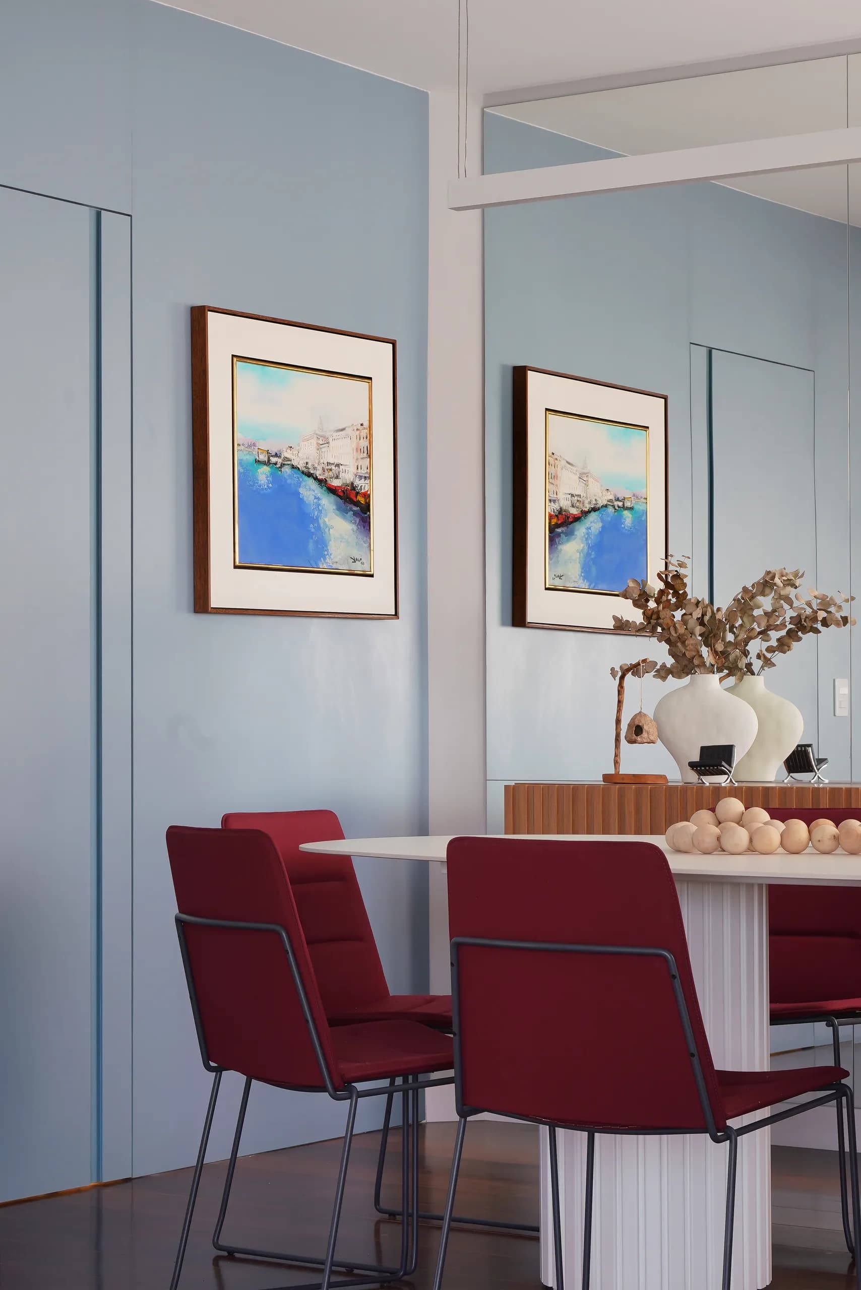 Sala de jantar com cadeiras estofadas em bordô, parede azul e quadros emoldurados